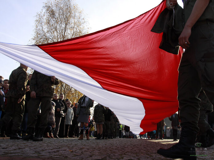 Zdjęcie dużej biało-czerwonej flagi trzymanej przez grupę osób