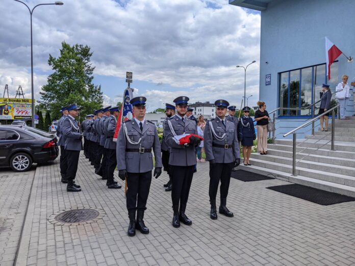 Trzej policjanci w galowych mundurach. Drugi od lewej trzyma złożoną flagę Polski