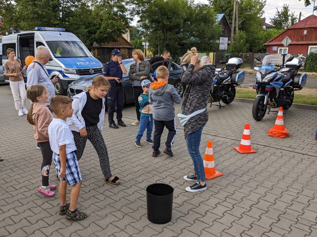 Grupa dorosłych i dzieci bawi się na tle policyjnych motocykli i samochodów