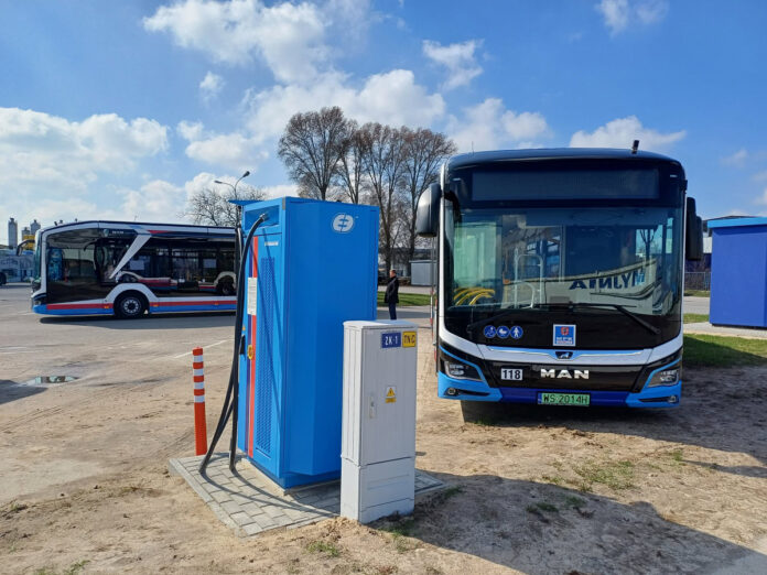 Na zdjęciu na pierwszym planie stacja ładowania i autobus elektryczny ustawiony przodem