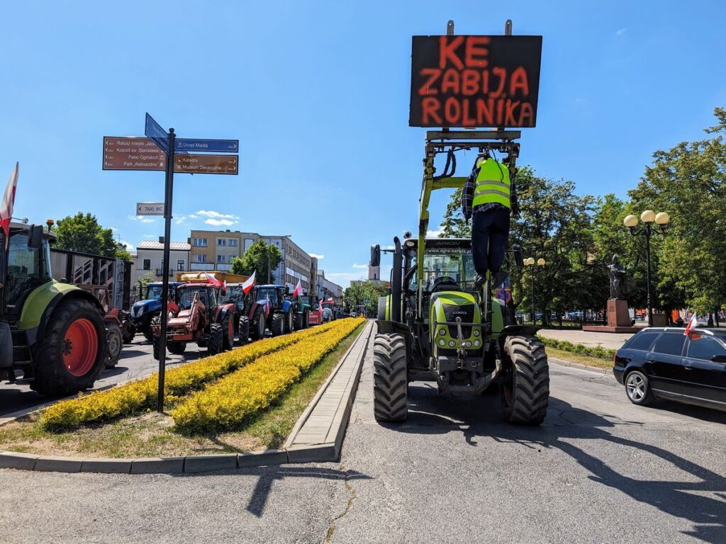 Kukła zawieszona na ciągniku z plakatem "KE zabija rolnika"