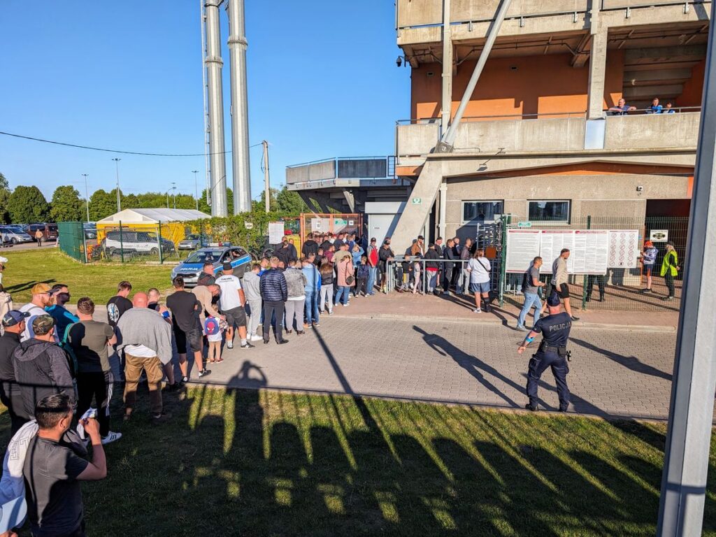 Kibice stoją w kolejce, pod stadionem, aby kupić bilet na mecz