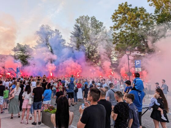 Dziesiątki osób stoją z odpalonymi niebieskimi i czerwonymi racami