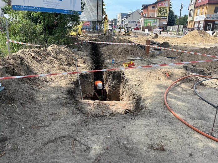 Wykopaliska w środku drogi, ogrodzone taśmą, w dole pracuje archeolog