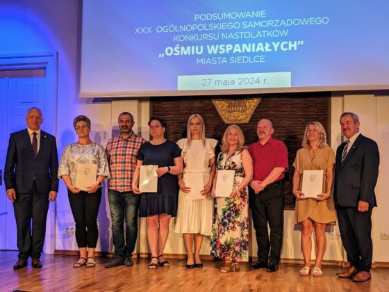 Dorośli ludzie stoją w jednym rzędzie trzymając w dłoniach listy gratulacyjne