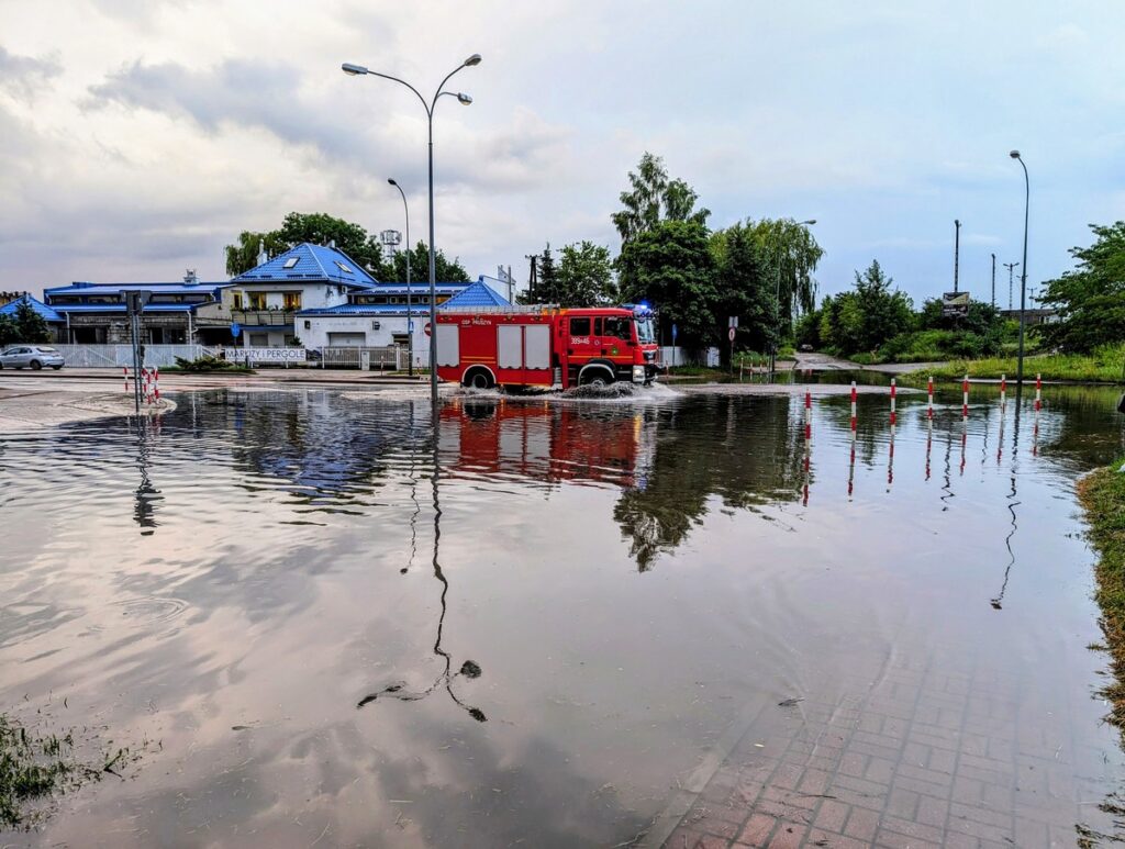 Zalana ulica, w tle jadący wóz strażacki