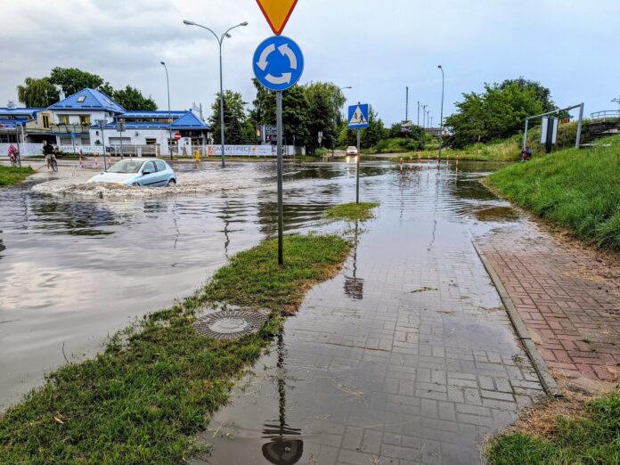 Zalana ulica i chodnik, samochód ledwo przejeżdża przez wodę