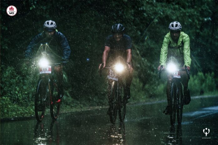 Trzej rowerzyści jadą wieczorową porą w deszczu