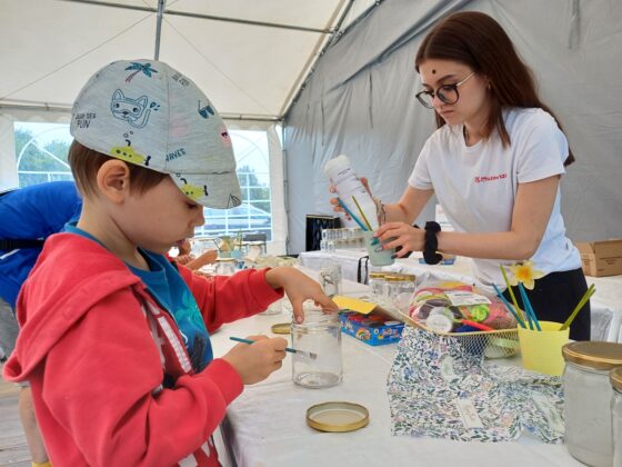 Chłopiec w czerwonej bluzie malujący słoik. W tle kobieta