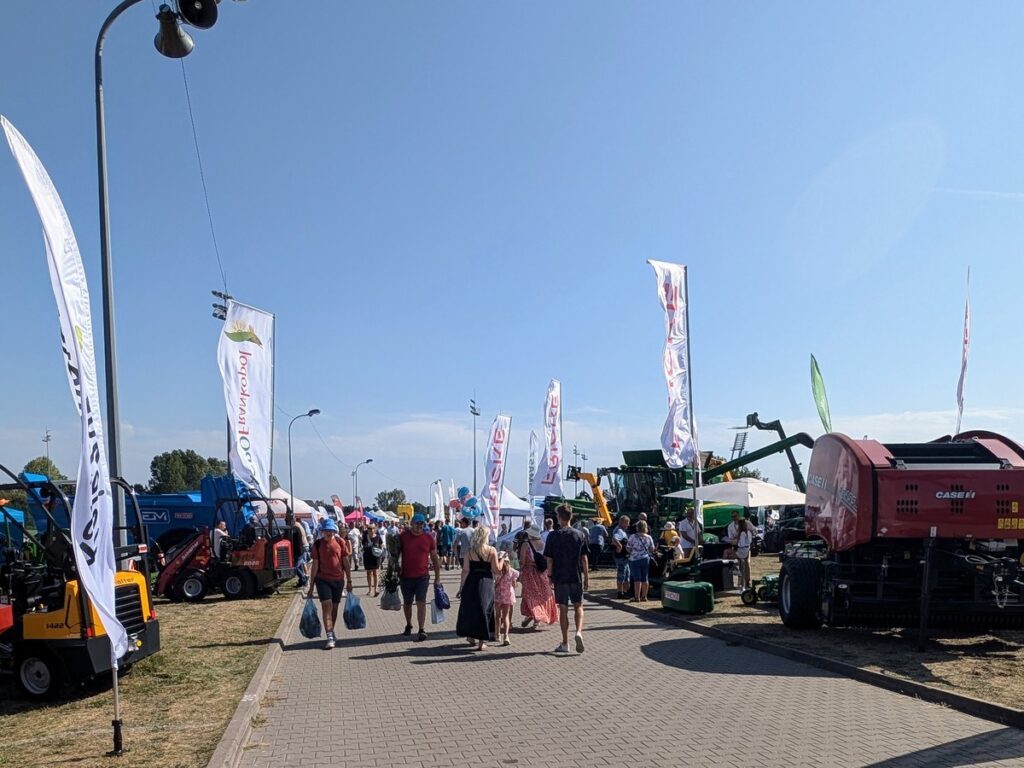 Dziesiątki osób idące alejką, po obu jej stronach stoją maszyny rolnicze