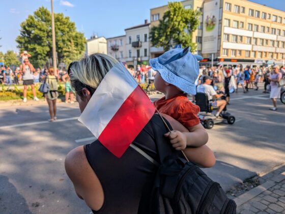 Dziecko z małą bało-czerwoną flagą w dłoni trzymane przez kobietę