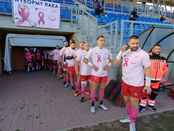 Zawodnicy rugby w koszulkach promujących samobadanie piersi wychodzą na boisko