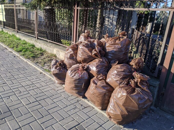 Brązowe worki z odpadami leżące przy chodniku.