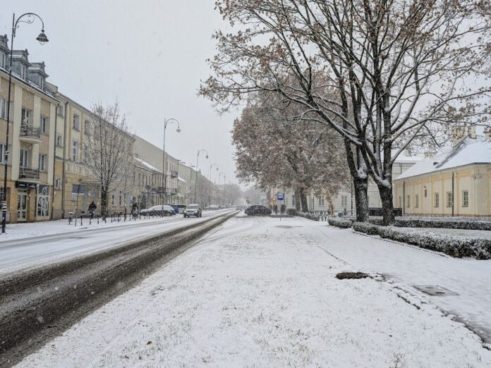 Ulica w zimowej scenerii, pokryta śniegiem, z samochodami i drzewam