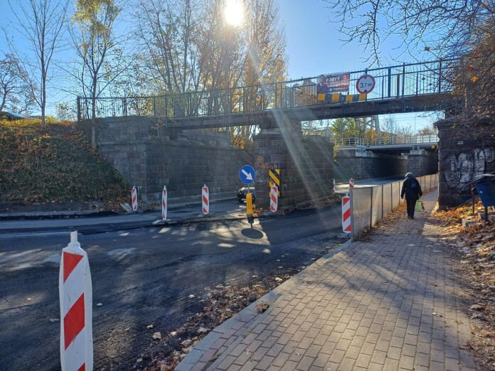 Most nad drogą z przechodniem idącym obok, otoczony zielenią.