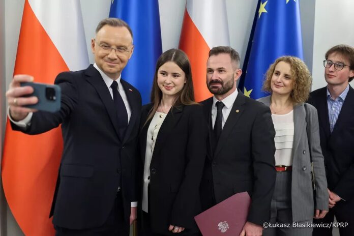 Grupa pięciu uśmiechniętych osób, jeden z trzech mężczyzn robi selfie.