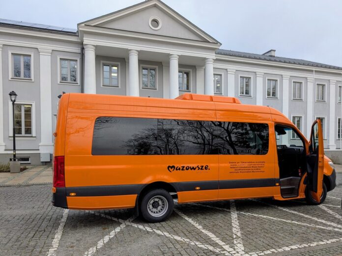 Pomarańczowy bus stoi na tle budynku z kolumnami.