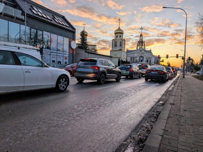 Samochody jadą zimowym porankiem ulicą w jednym kierunku.