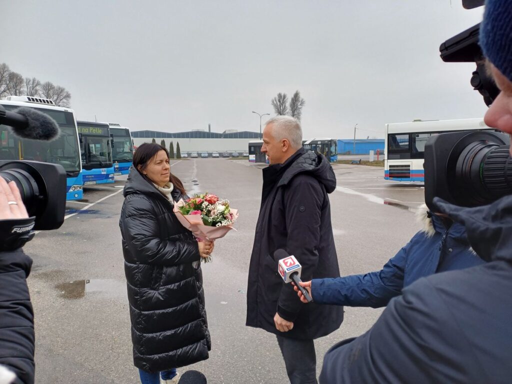 Mężczyzna i kobieta stoją przed autobusem, kobieta trzyma kwiaty