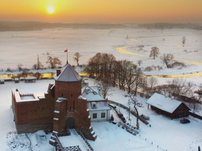 Zimowy krajobraz z zamkiem w tle, uchwycony z powietrza, ze śniegiem i drzewami.