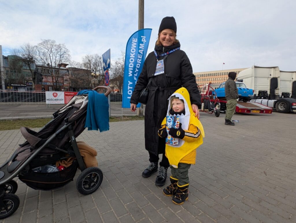 Kobieta i dziecko stoją obok wózka dziecięcego, uśmiechając się i ciesząc wspólnym czasem na świeżym powietrzu.